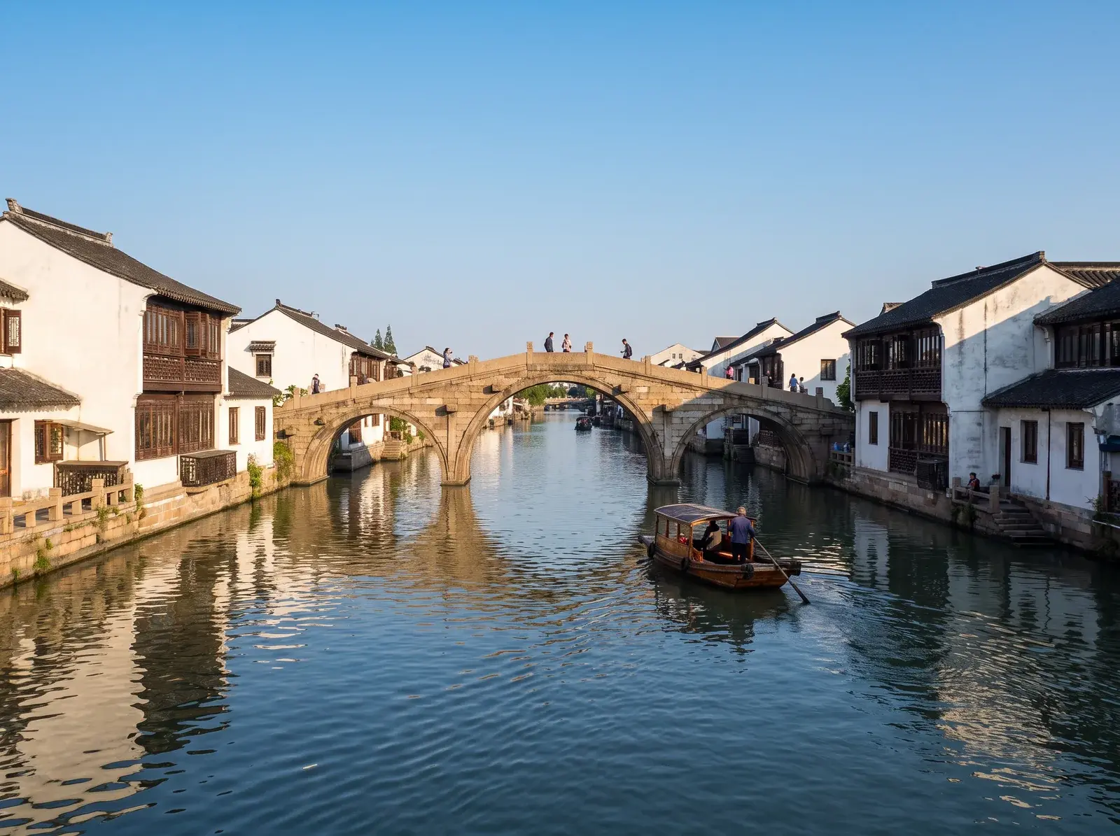 Zhujiajiao'da beyaz duvarlı evlerin arasındaki kanalı taş kemerli köprü geçiyor, suda üstü örtülü bir tekne ilerliyor.