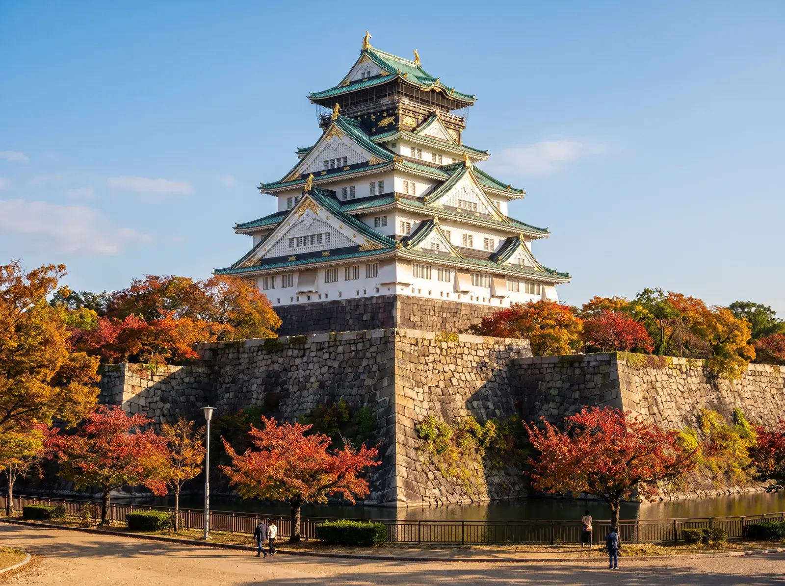 Taş surların üzerinde beyaz duvarlı, yeşil çatılı Osaka Kalesi.
