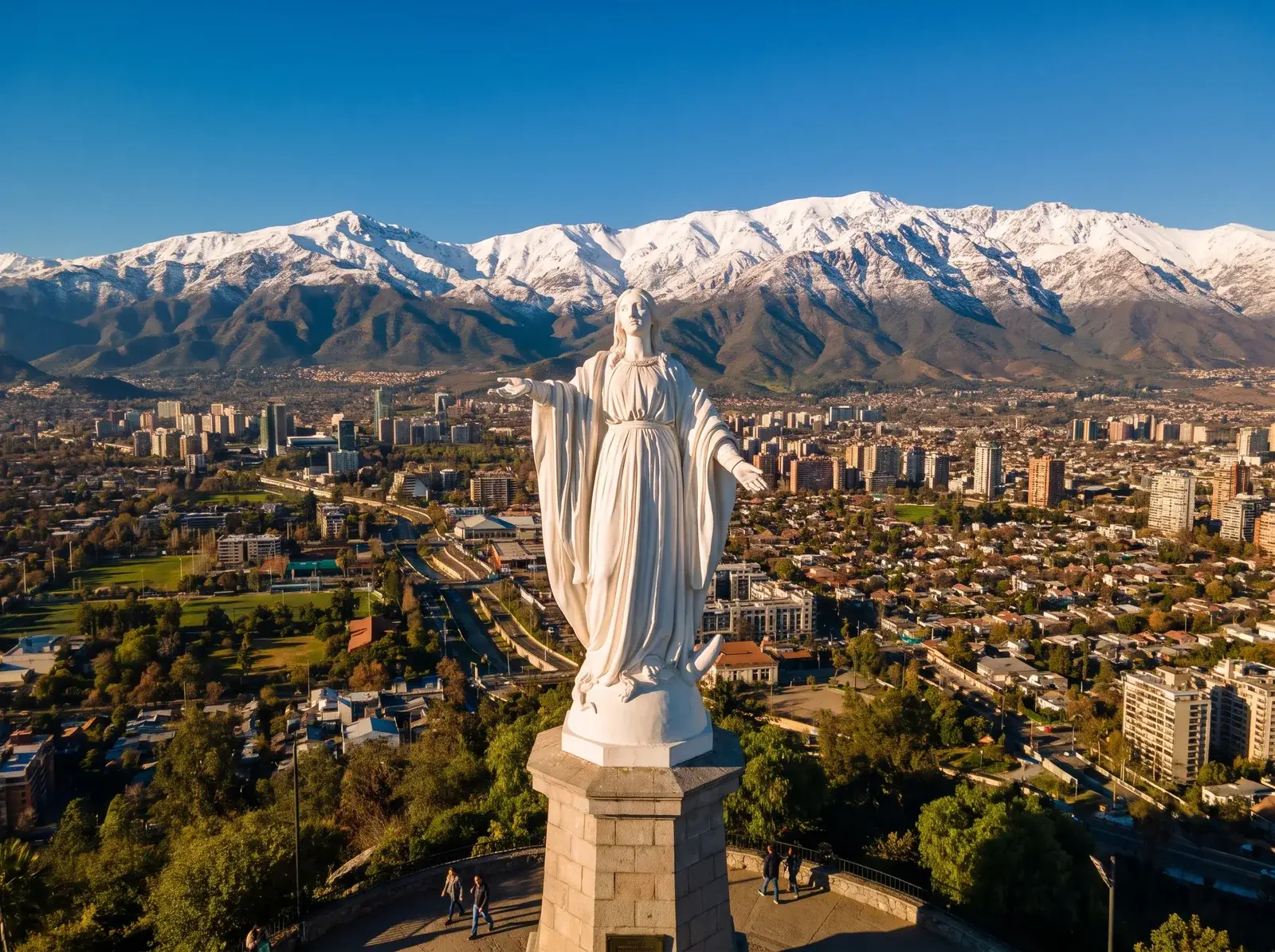 Cerro San Cristóbal'deki beyaz Meryem heykelinin arkasında Santiago binaları ve karla kaplı dağ sırası uzanıyor.
