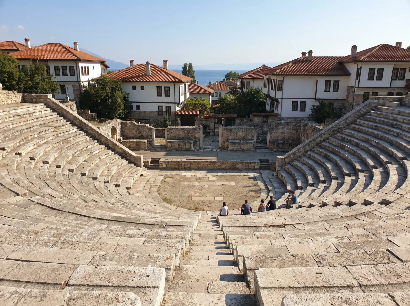 Ohrid Eski Şehir'de antik tiyatronun yarım daire biçimli taş sıralarının ardında beyaz evler ve göl görülüyor.