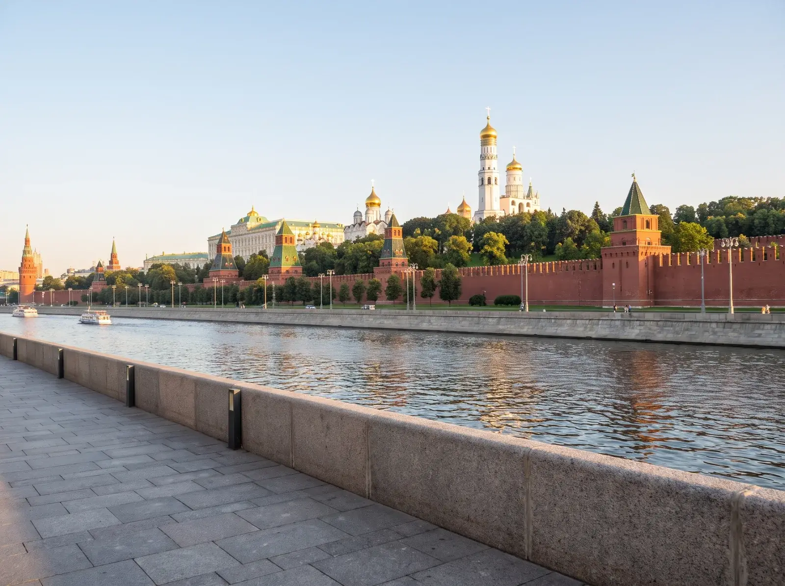 Kremlin'in kırmızı surları, kuleleri ve altın kubbeli beyaz yapıları, nehrin karşı kıyısında ağaçlar arasında uzanıyor.