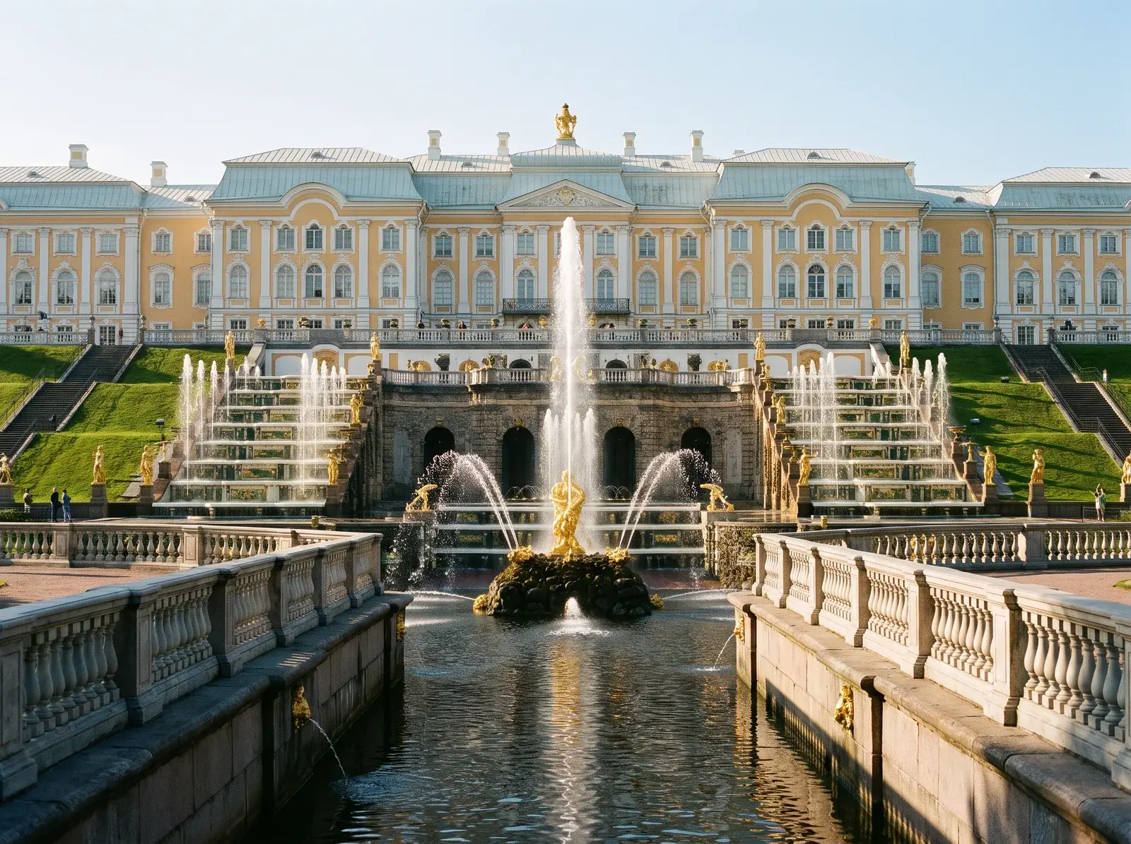 Peterhof Sarayı önünde altın renkli heykeller, basamaklı çeşmeler ve taş korkuluklarla çevrili su kanalı uzanıyor.