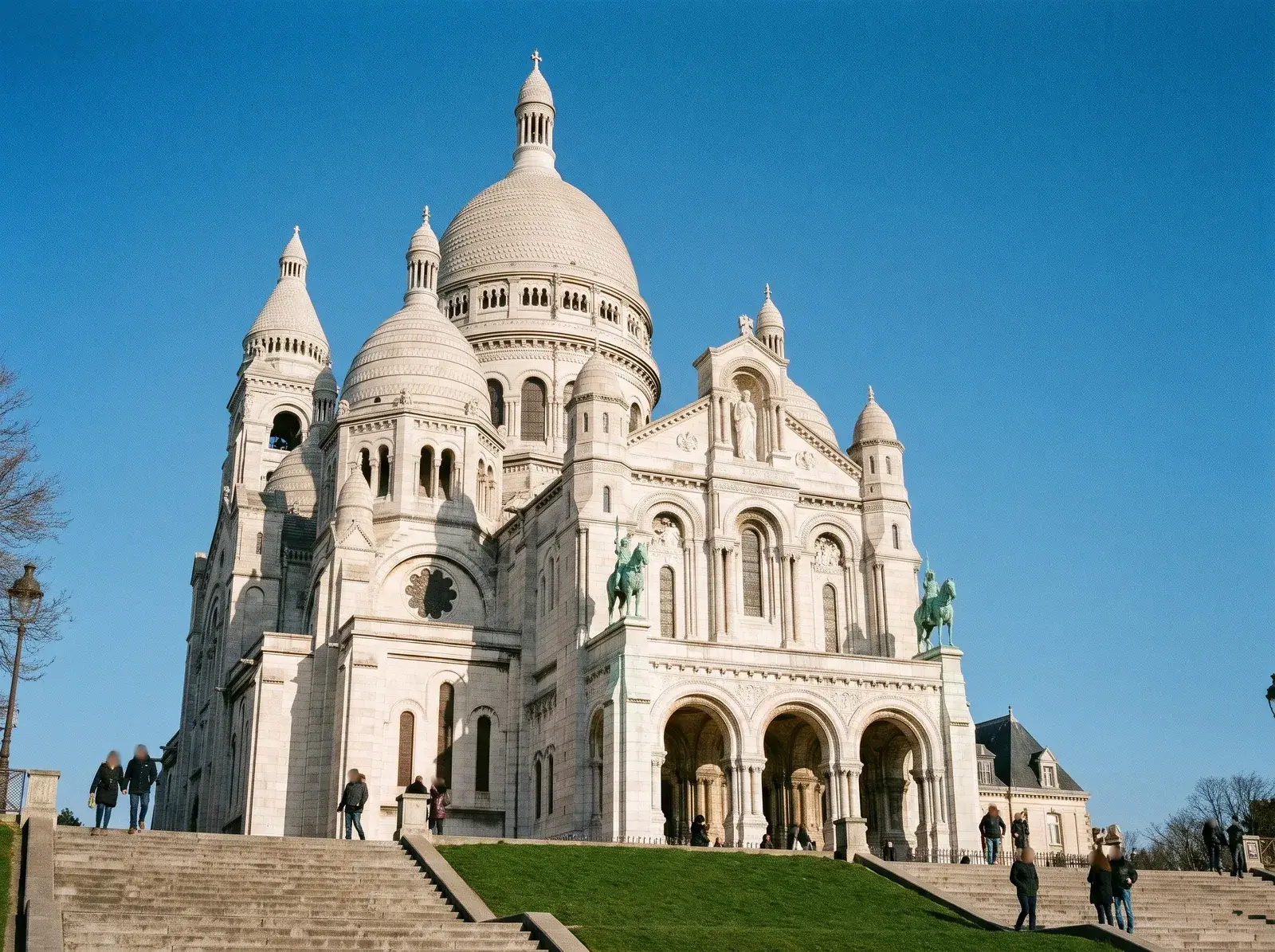 Montmartre tepesindeki Sacré-Cœur'ün beyaz kubbeleri, önündeki merdivenler ve çimenlik alan.
